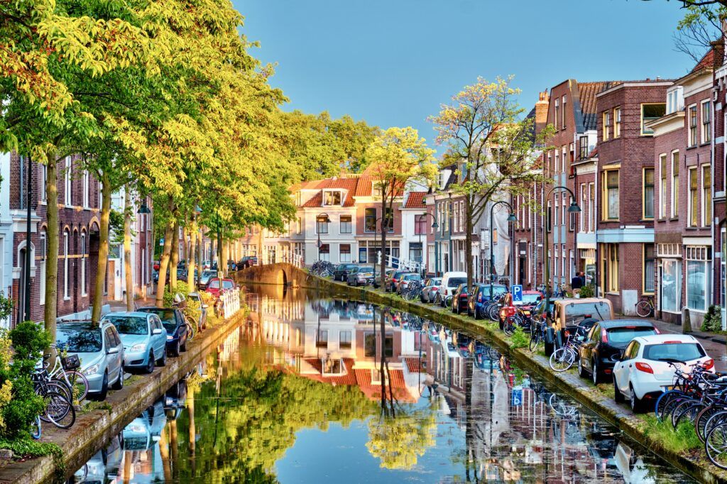 Delft canal with old houses and cars parked along on sunset.