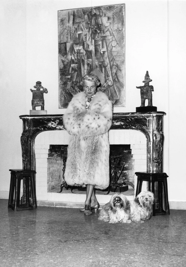 Peggy Guggenheim standing in her fur in front of a Braque paintings