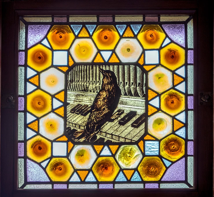 stained glass window with a bird playing a piano in El Capricho