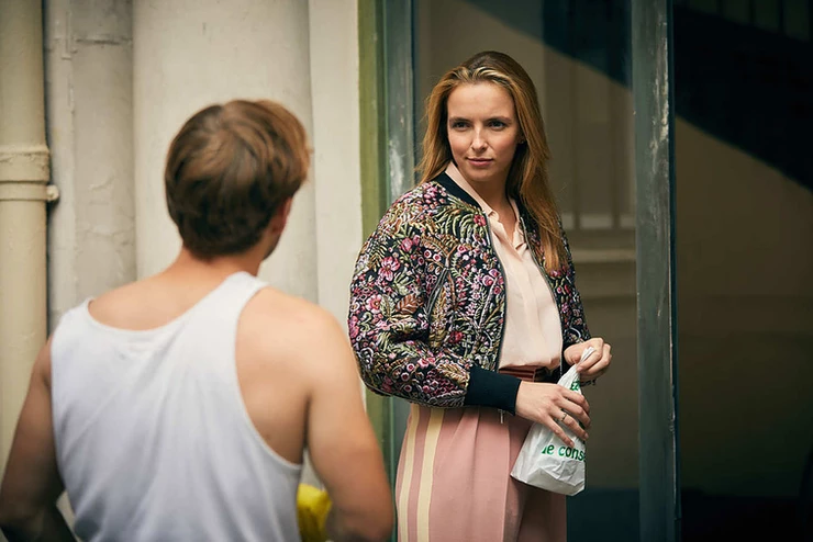Villanelle, wearing a hip Phillip Lim flowered bomber jacket, meets her awestruck neighbor Sebastian coming home to her apartment