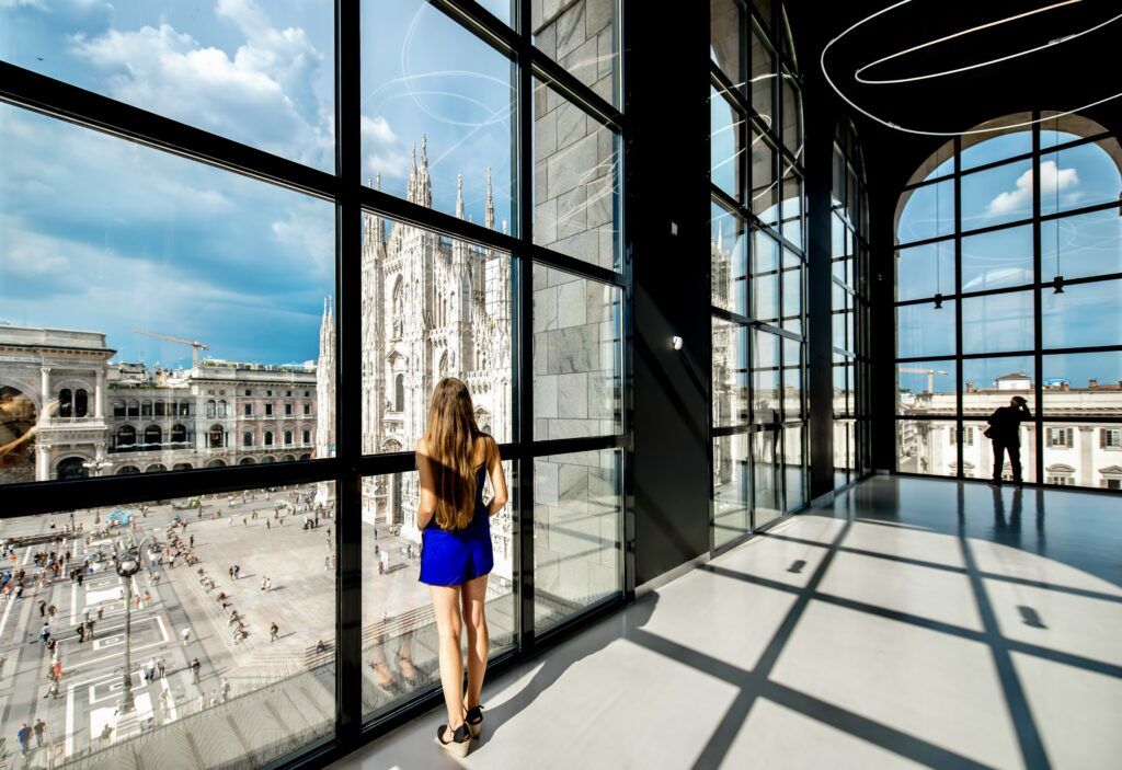 Woman stand in the big hall with windows and great view on Duomo cathedral in Novecento museum. Novecento is a museum of modern art in Milan